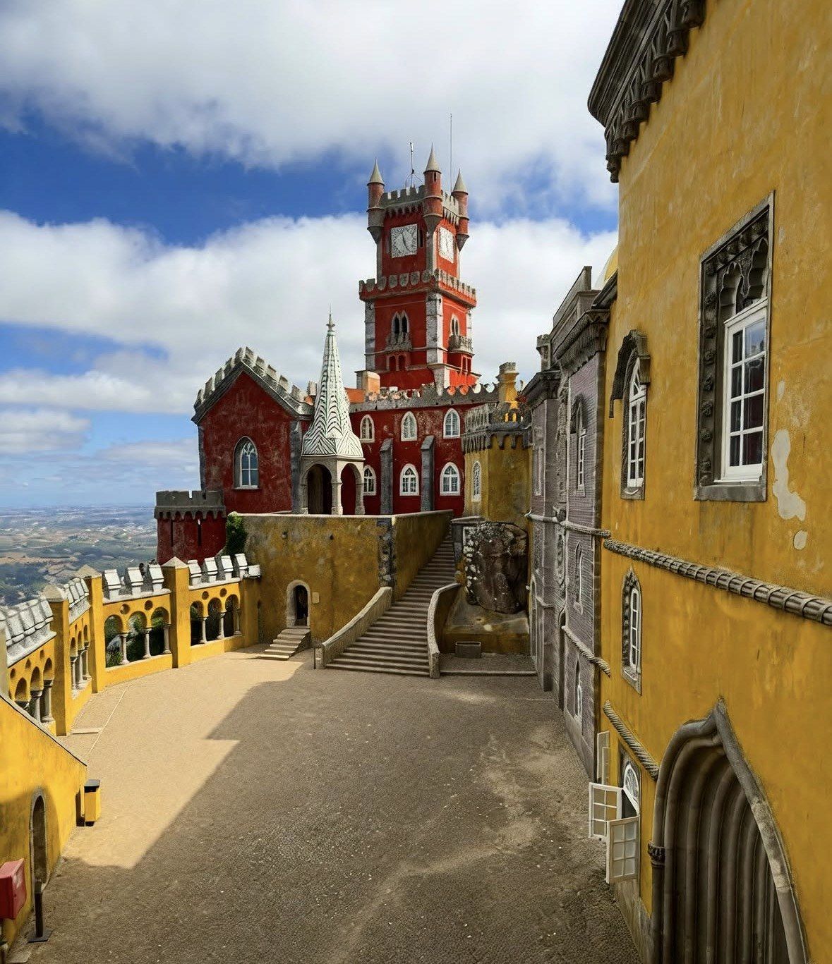Pena Palace clock tower above the sandy upper courtyard under clouds