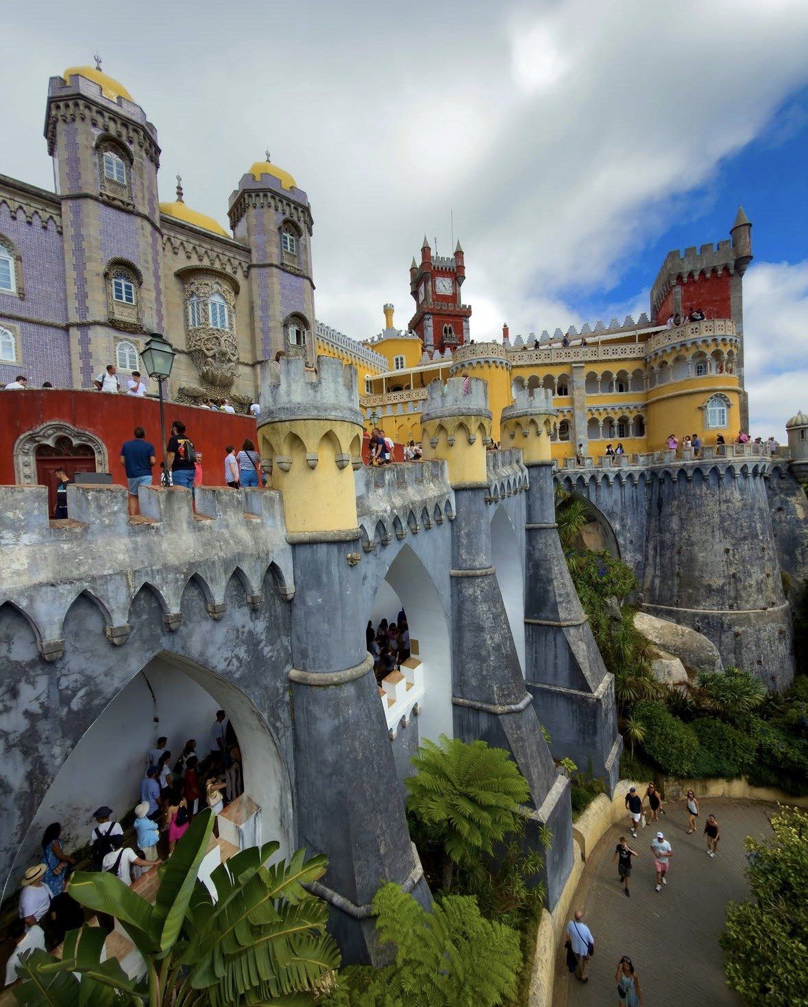 Visitors crossing the grey arched viaduct beneath Pena Palace terraces