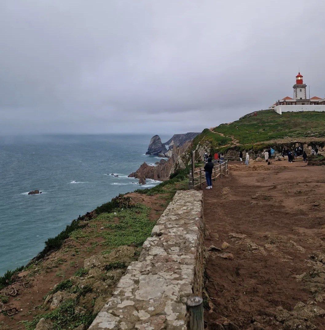 Misty clifftop path toward the lighthouse above a grey Atlantic