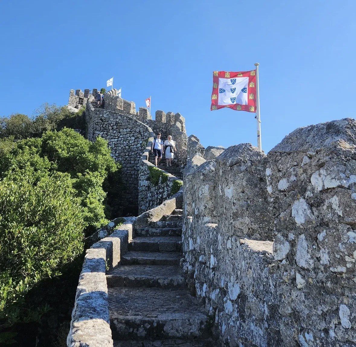 Two walkers descending steep castle steps beside a royal banner