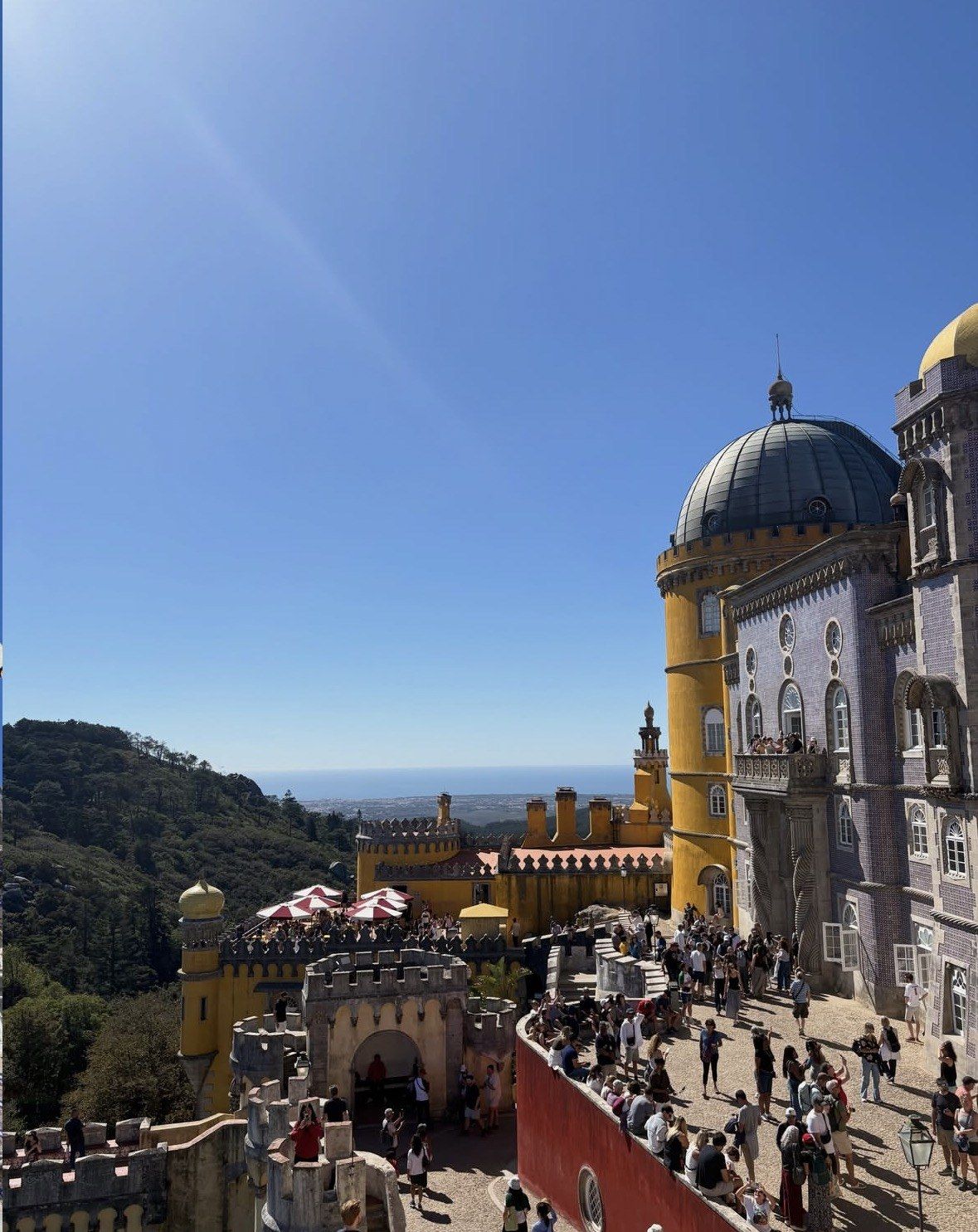 Crowded sunlit terrace at Pena Palace with the distant sea horizon